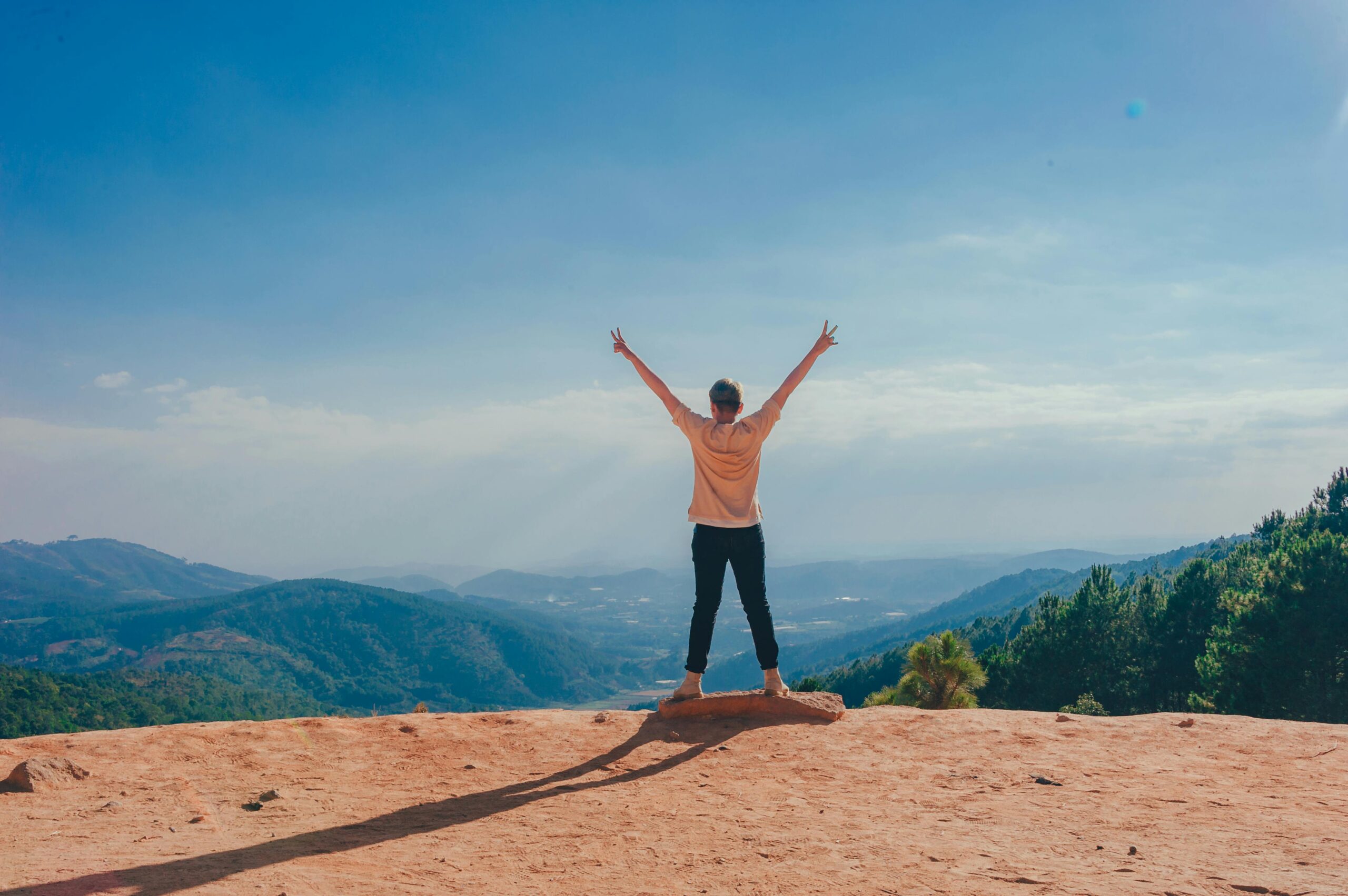 View from behind of a person standing at the top of a cliff with their arms up in celebration